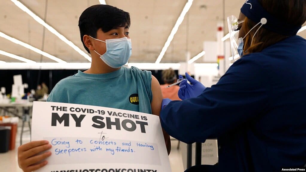 Un niño de 13 años muestra un cartel de apoyo a la vacunación mientras recibe su primera dosis en Illinois, en mayo de 2021. | Foto: VOA/AP.